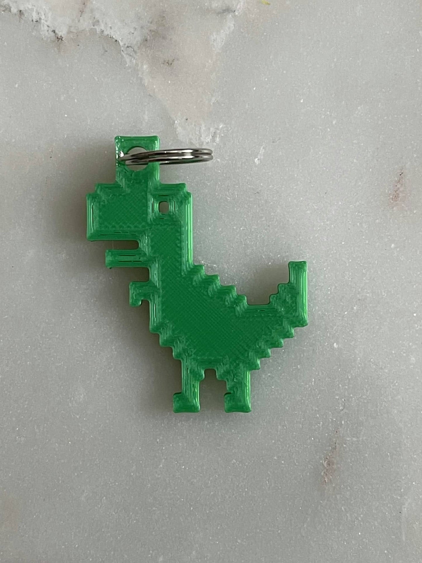 8-Bit Dino Keyring in green on a white marble background.